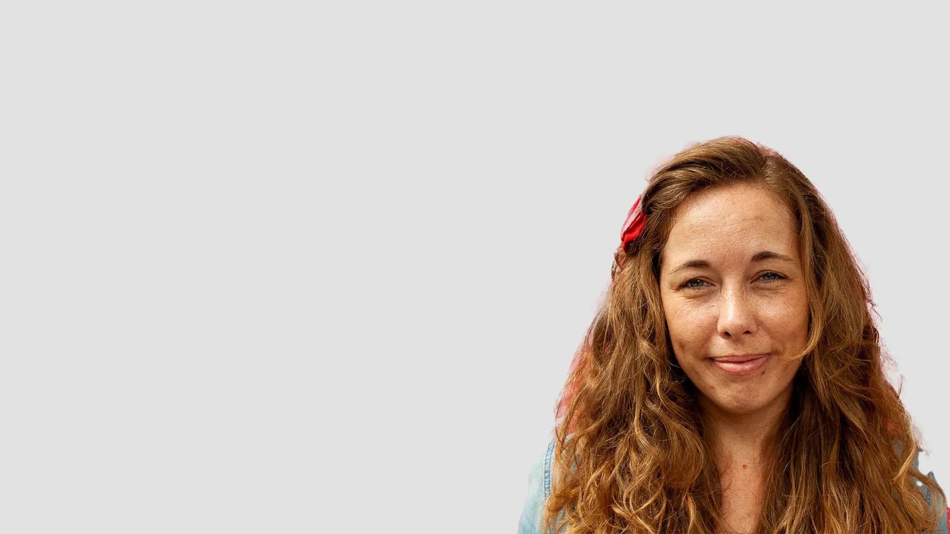 Smiling woman with curly hair wearing a red bow in her hair.