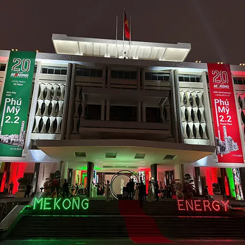 Façade illuminée d’un bâtiment avec des bannières rouges et vertes pour l’événement des 20 ans de Mekong Energy, et un tapis rouge menant à l’entrée.