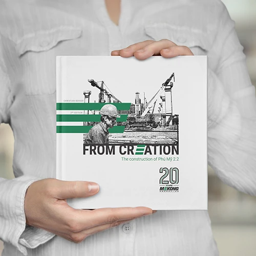 Livre intitulé "From Creation – The Construction of Phú Mỹ 2.2", célébrant les 20 ans de Mekong Energy, tenu par une personne en chemise blanche.